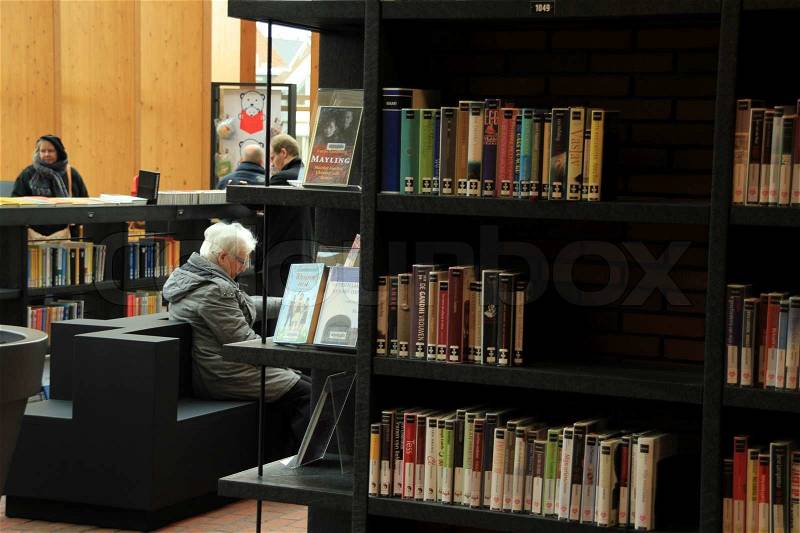 Reading a book in the municpal library between all kind of books in different colours in order, stock photo