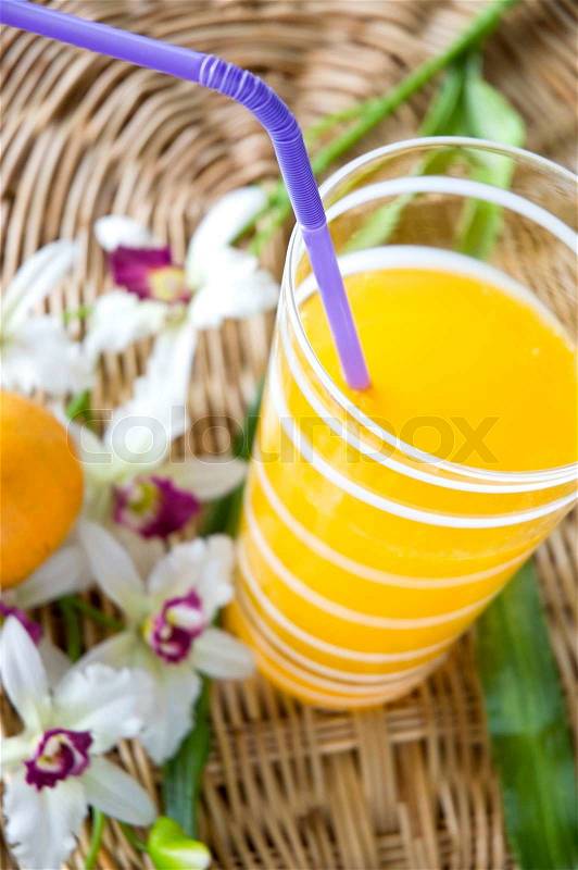 Glass of orange juice with drinking straw put beside orchid, stock photo