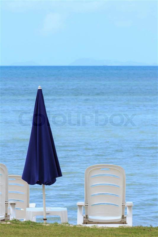 Sea view with blue umbrella and white chairs, stock photo