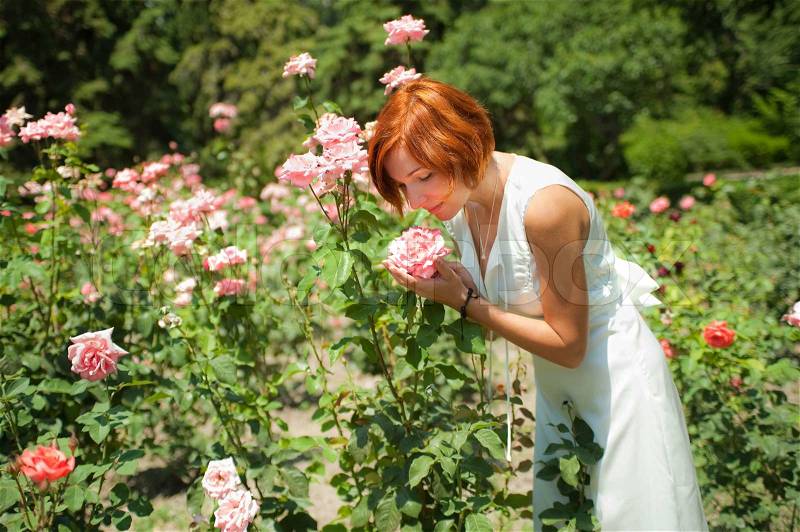 Beautiful young woman in a garden of roses at sunny summer day, stock photo