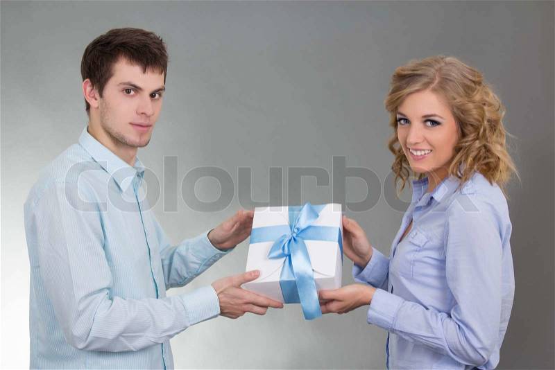 Young man giving a gift to his beautiful girlfriend over grey, stock photo