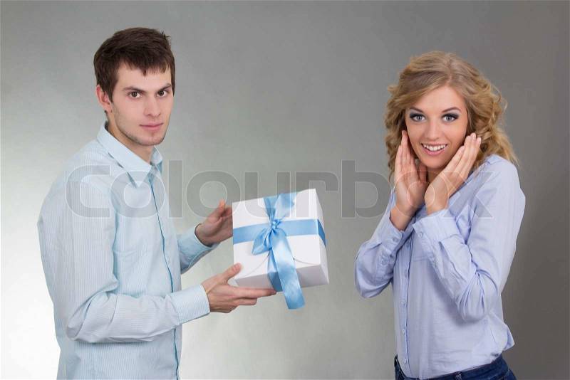 Young man with gift and surprised girlfriend over grey, stock photo