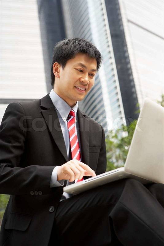 Chinese Businessman Working On Laptop Outside Office, stock photo