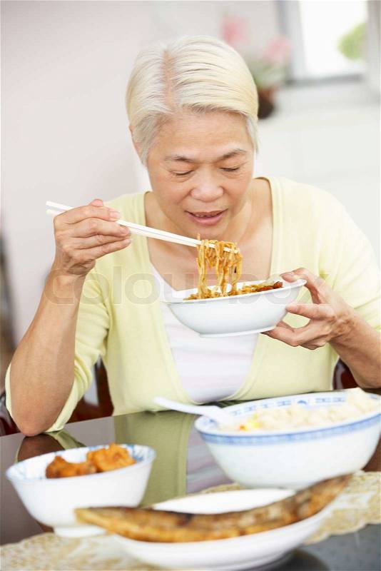 Senior Chinese Woman Sitting At Home Eating Meal, stock photo