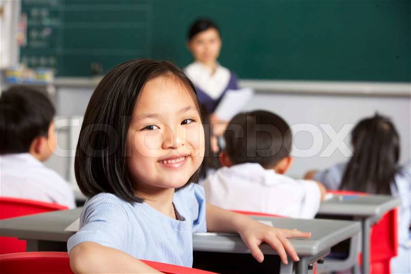 Portrait Of Female Pupil Working At Desk In Chinese School Classroom, stock photo