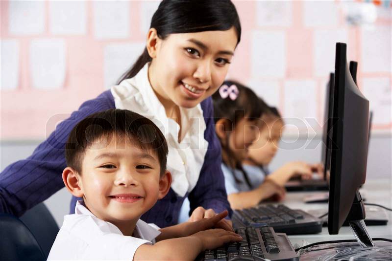 Teacher Helping Student During Computer Class In Chinese School Classroom, stock photo