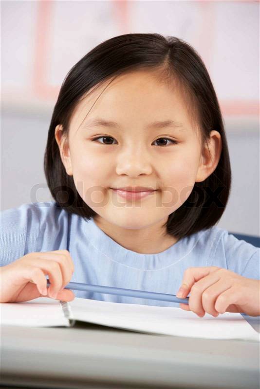 Female Student Working At Desk In Chinese School Classroom, stock photo