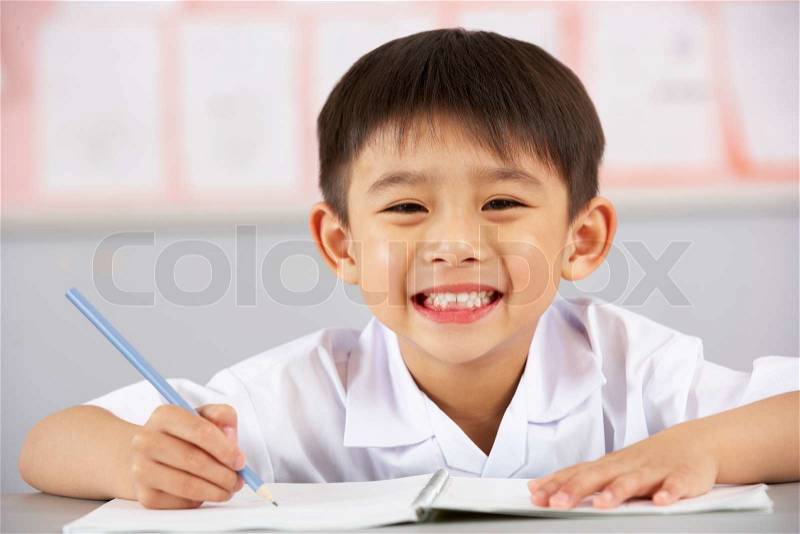 Male Student Working At Desk In Chinese School Classroom, stock photo
