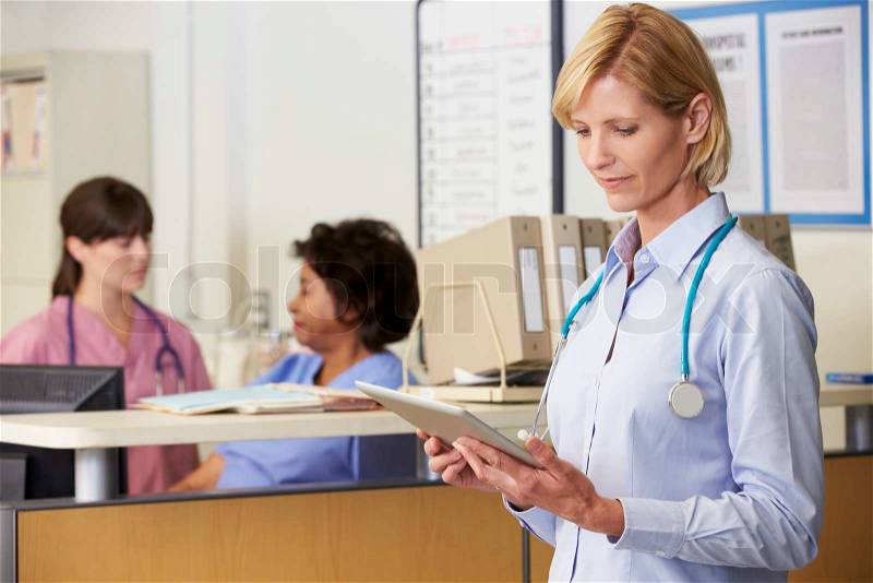 Female Doctor Reading Patient Notes At Nurses Station, stock photo