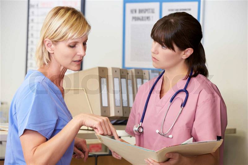 Two Nurses Discussing Patient Notes At Nurses Station, stock photo