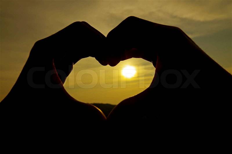 Heart silhouette by hand on sunrise background, stock photo