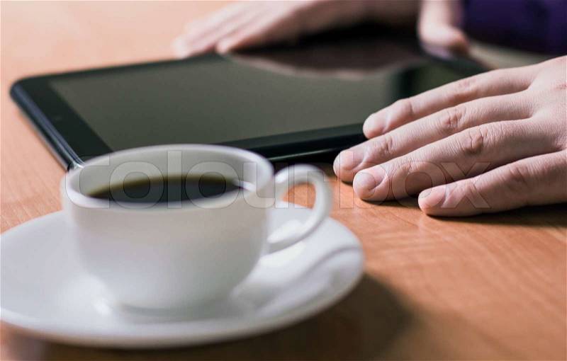 A man holding a cup of coffee and working on a Tablet PC, stock photo