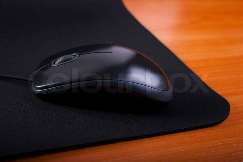Black computer mouse and black pad on wooden table, stock photo