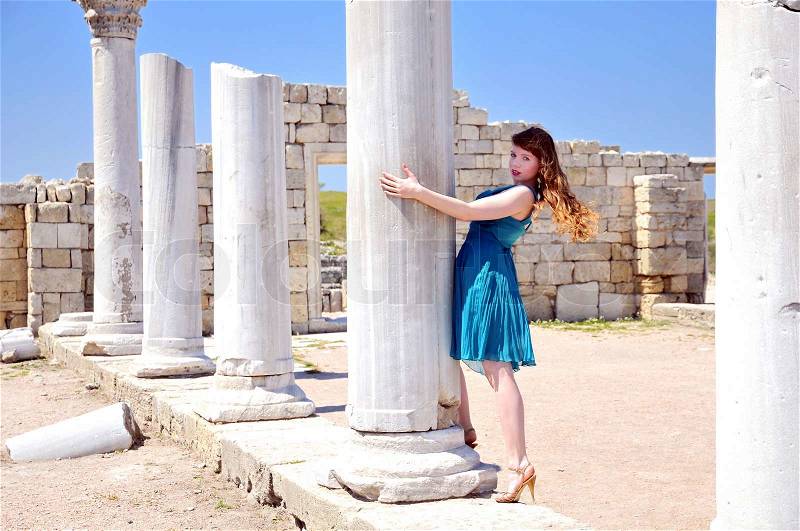 Young fashion model wearing sexy blue dress and high-heel shoes standing close to the Ancient Ruins, stock photo