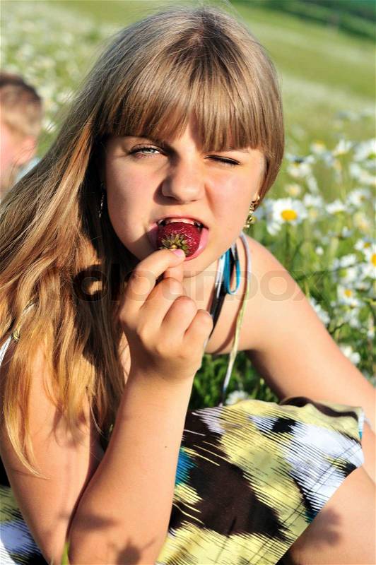 Teen funny girl eating fresh strawberry outdoors, stock photo