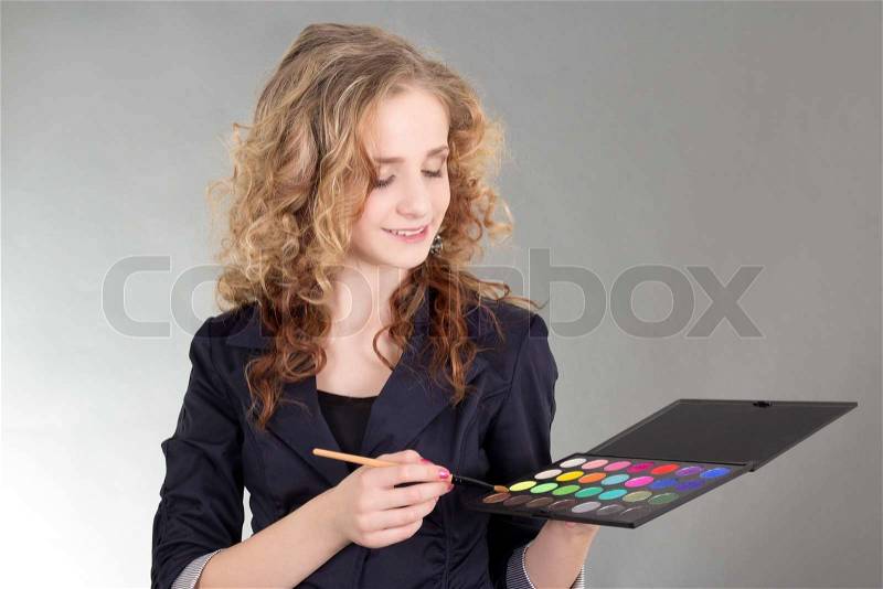 Young beautiful woman with make up brushes and palette over grey, stock photo