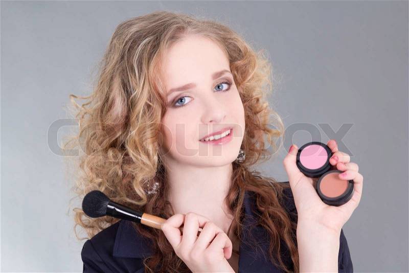 Young attractive make up artist with brush over grey, stock photo