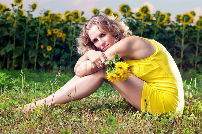 Beautiful girl in yellow clothes sits in the field with sunflowers, stock photo