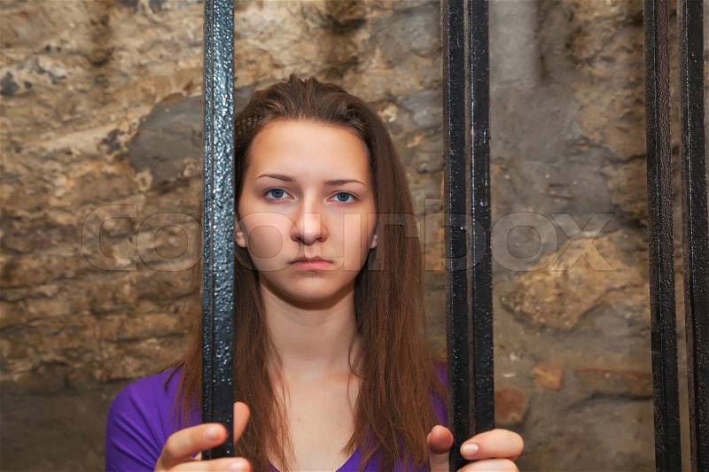 Young woman looking from behind the bars, stock photo