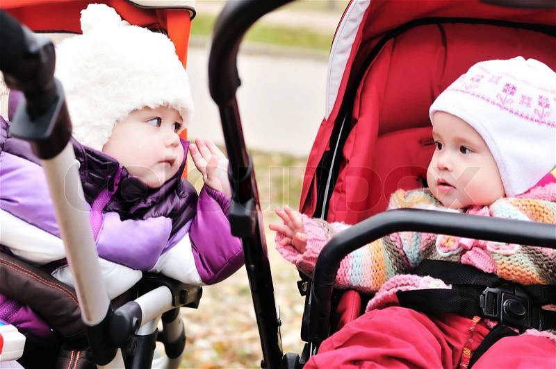 Two baby girls sitting in strollers and looking at each other, stock photo