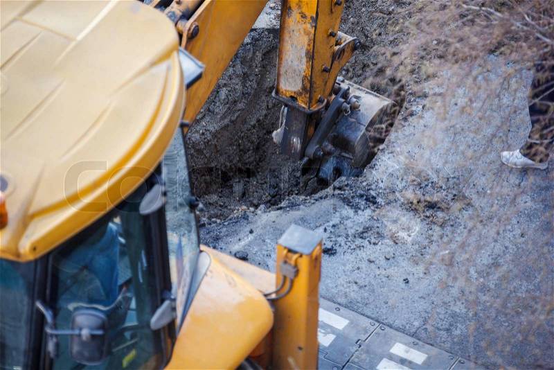 Excavator digging a hole, breaking street asphalt, repairing damaged water supply pipe, stock photo
