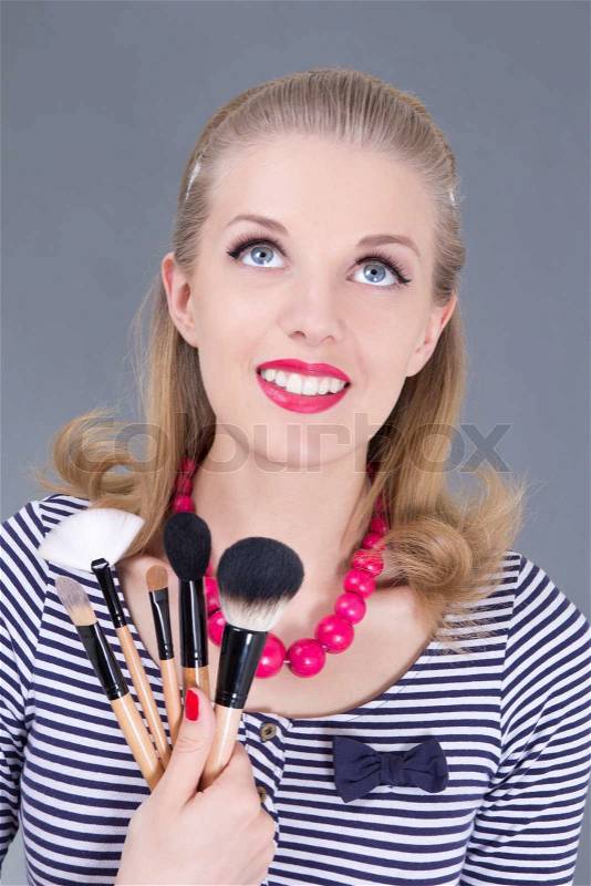 Young dreaming pinup woman with make up brushes, stock photo