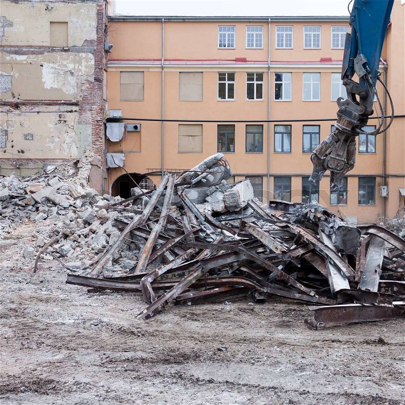 Demolition truck in action. Heap of rubble and a demolished building in the background, stock photo