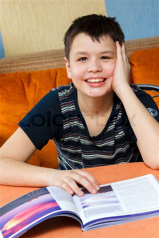 Happy little boy in black shirt sitting at a table and reading a book, stock photo