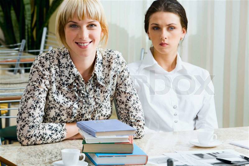Portrait of two confident students sitting at the table in the cafe after lecture, stock photo