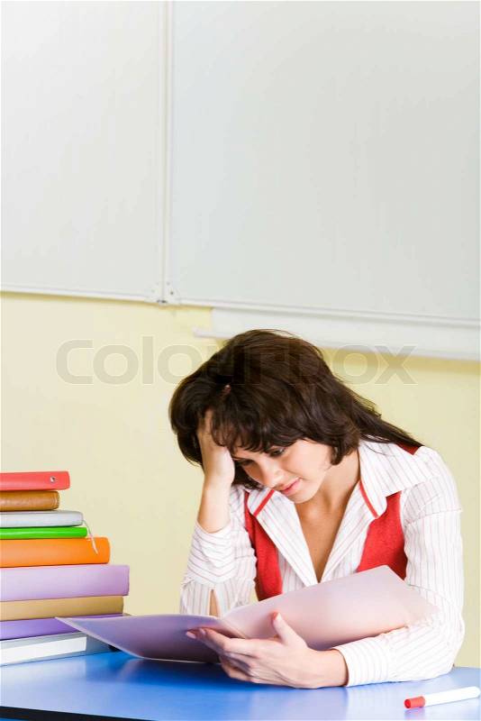 Image of tired student sitting at desk before textbook and looking into it with exhausted expression, stock photo