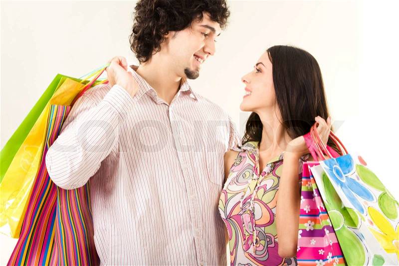 Portrait of a young couple carrying bags and looking at each other with smiles, stock photo