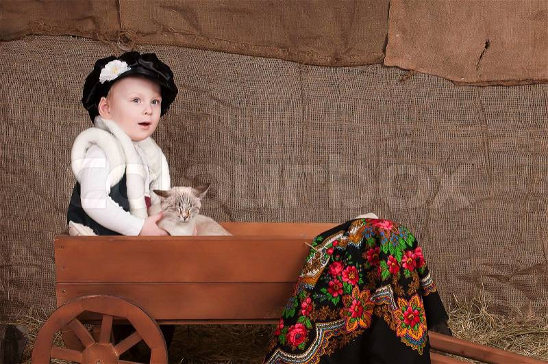Boy in national costume sits in a cart, playing with the cat, stock photo