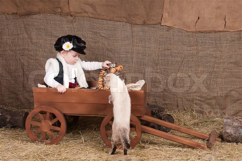 Boy in national costume sits in a cart, playing with the cat, stock photo
