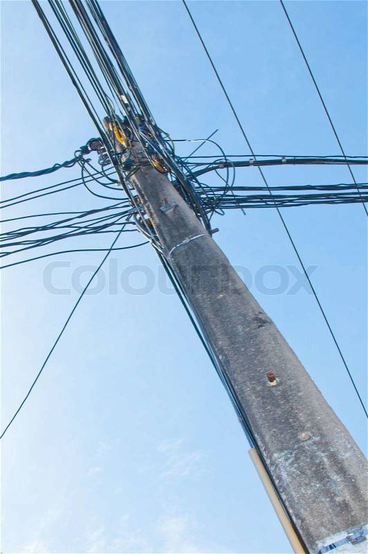 Energy and technology: electrical post by the road with power line cables, transformers and phone lines against bright blue sky providing copy space, stock photo