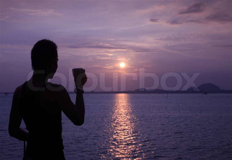 Silhouette of relaxing man having coffee while sun rising, stock photo