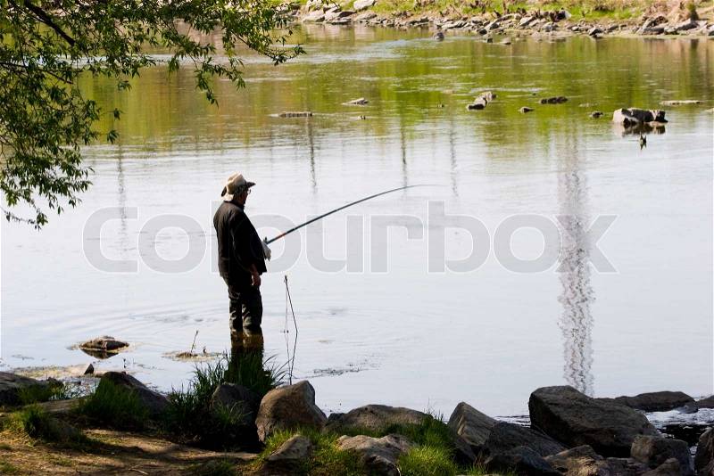 Photo of a fisher angling by the river in windless weather, stock photo