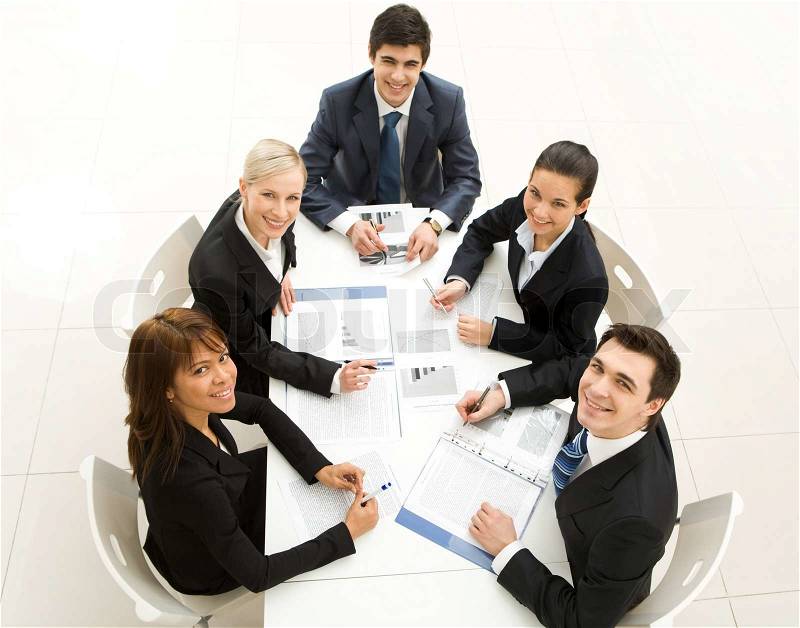 Several white collar workers sitting around table and looking upwards with smiles, stock photo