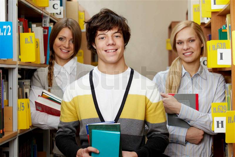 Portrait of happy guy with books looking at camera on background of his groupmates, stock photo