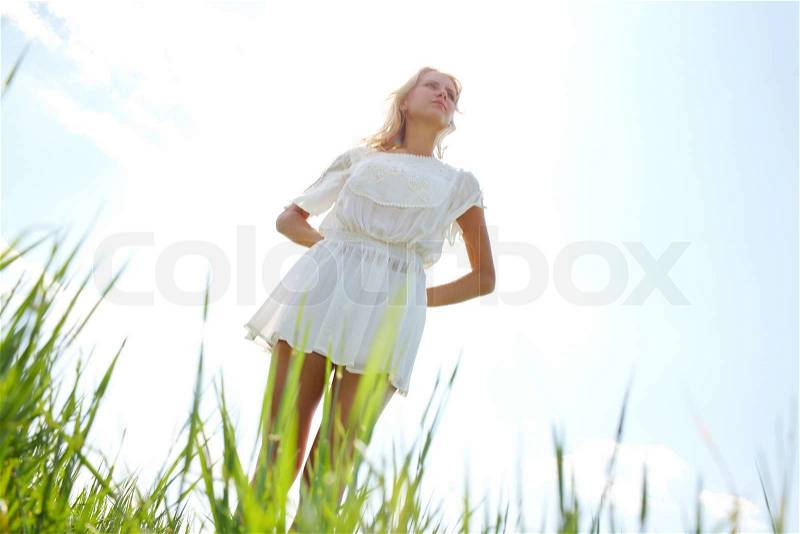 Photo of graceful female in white chiffon dress keeping her hands behind back with sunlight at background, stock photo