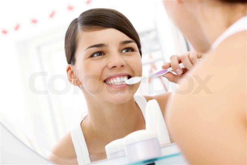 Image of pretty female brudhing her teeth in front of mirror in the morning, stock photo