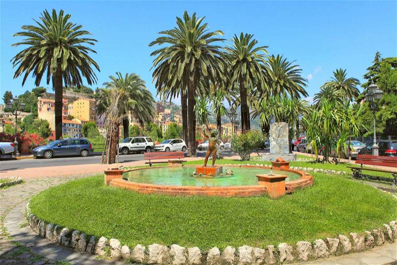 Little square with round small fountain and sculpture of the boy in the center surrounded my green lawn in Ventimiglia, Italy, stock photo