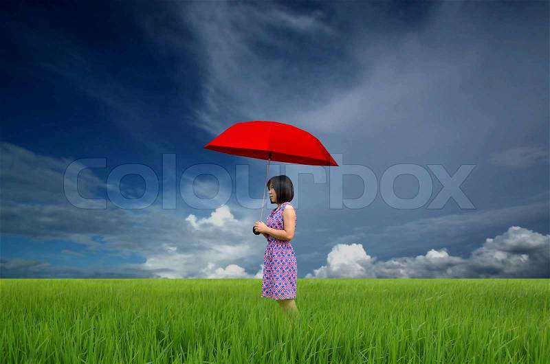 Young woman with red umbrella in a green field under rain, stock photo