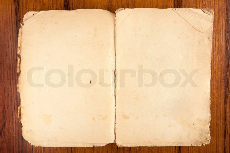 Old opened softcover book with yellowed pages on a wooden background, stock photo