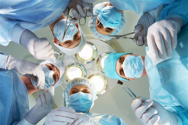 Below view of surgeons holding medical instruments in hands and looking at patient, stock photo