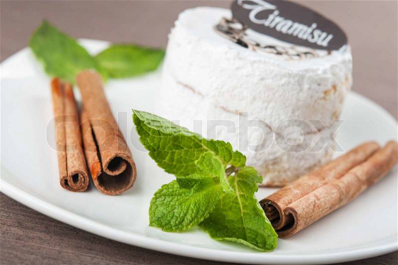 Tiramisu cake on white plate with mint and cinnamon, stock photo