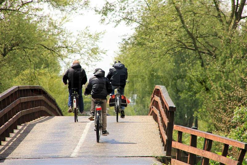 The three boyfriends, one with pannier, are biking over the brown bridge and going home from school, stock photo