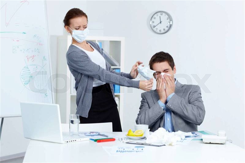 Image of businessman sneezing while his partner in mask offering him to put on one in office , stock photo