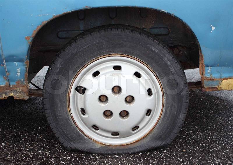 Flat tire on rusty blue van parked on asphalt, stock photo