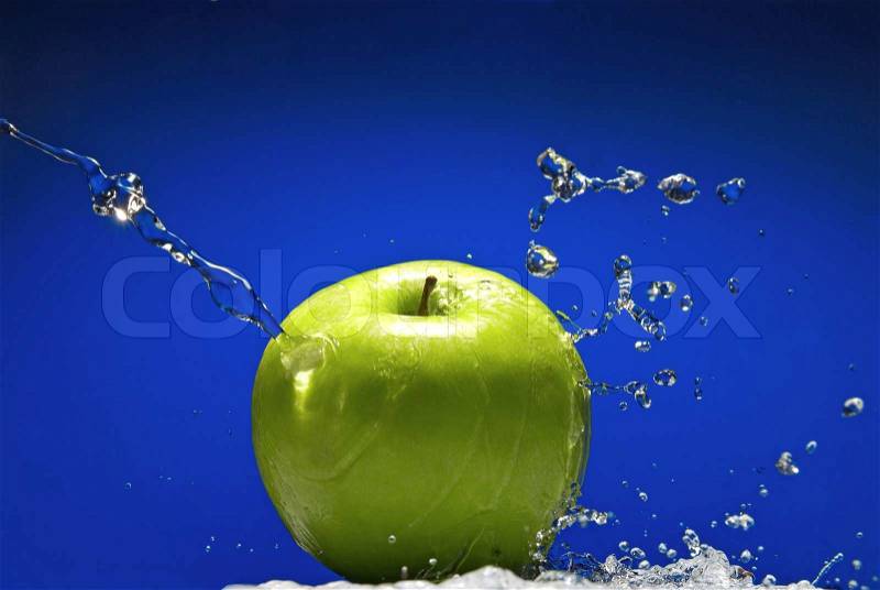 Green apple with water splash on blue background, stock photo