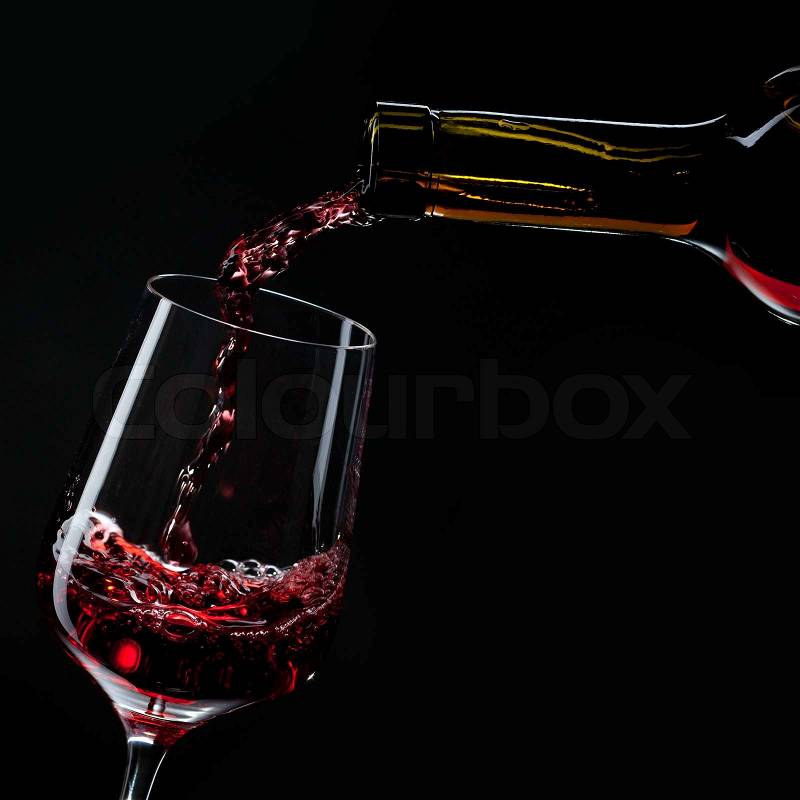 Red wine pouring into wine glass isolated on black, stock photo